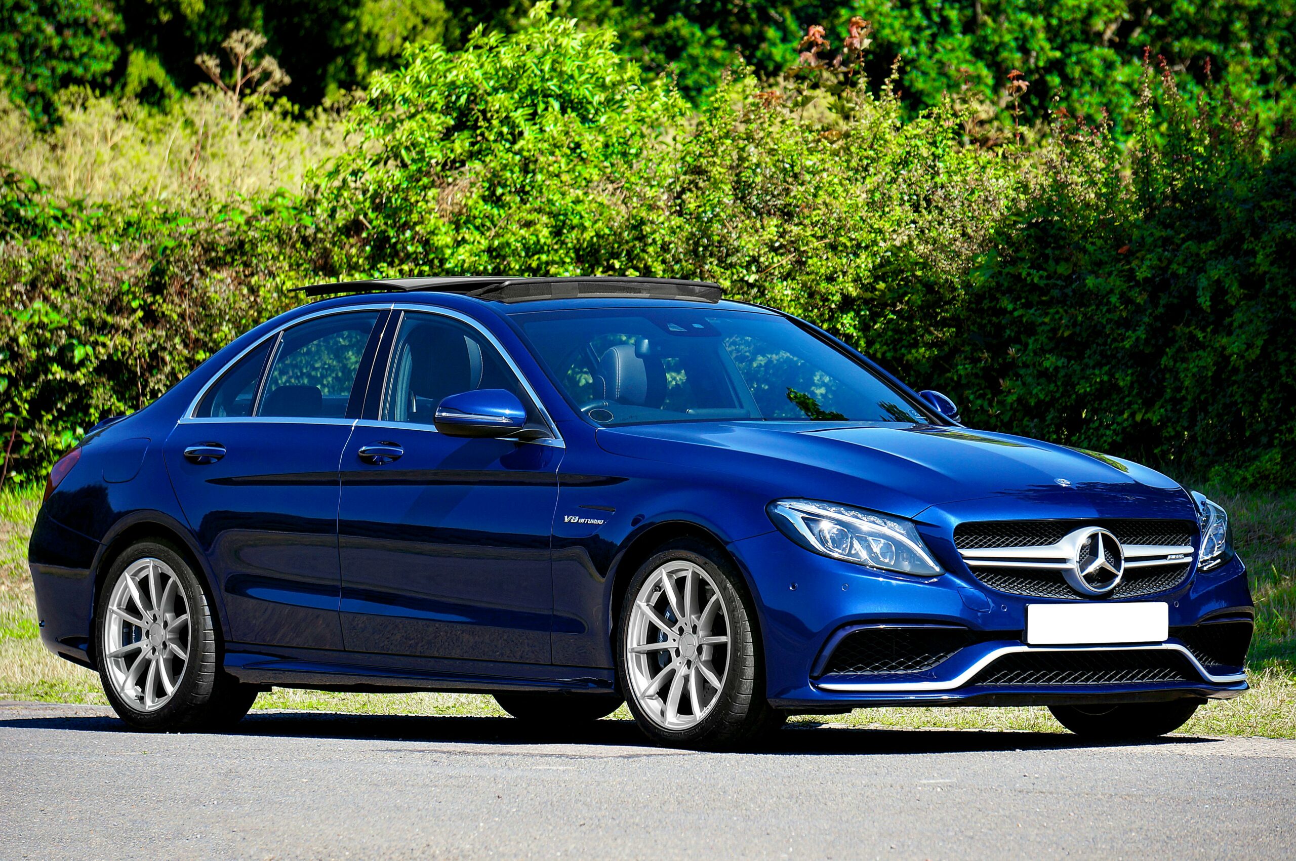 A stylish blue Mercedes-Benz parked outdoors with lush green bushes in the background.